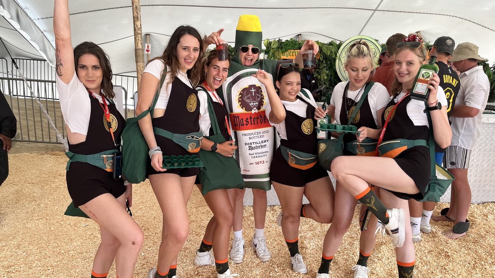 Six Jägermeister ambassadors laughing around a person in a Jägermeister bottle costume